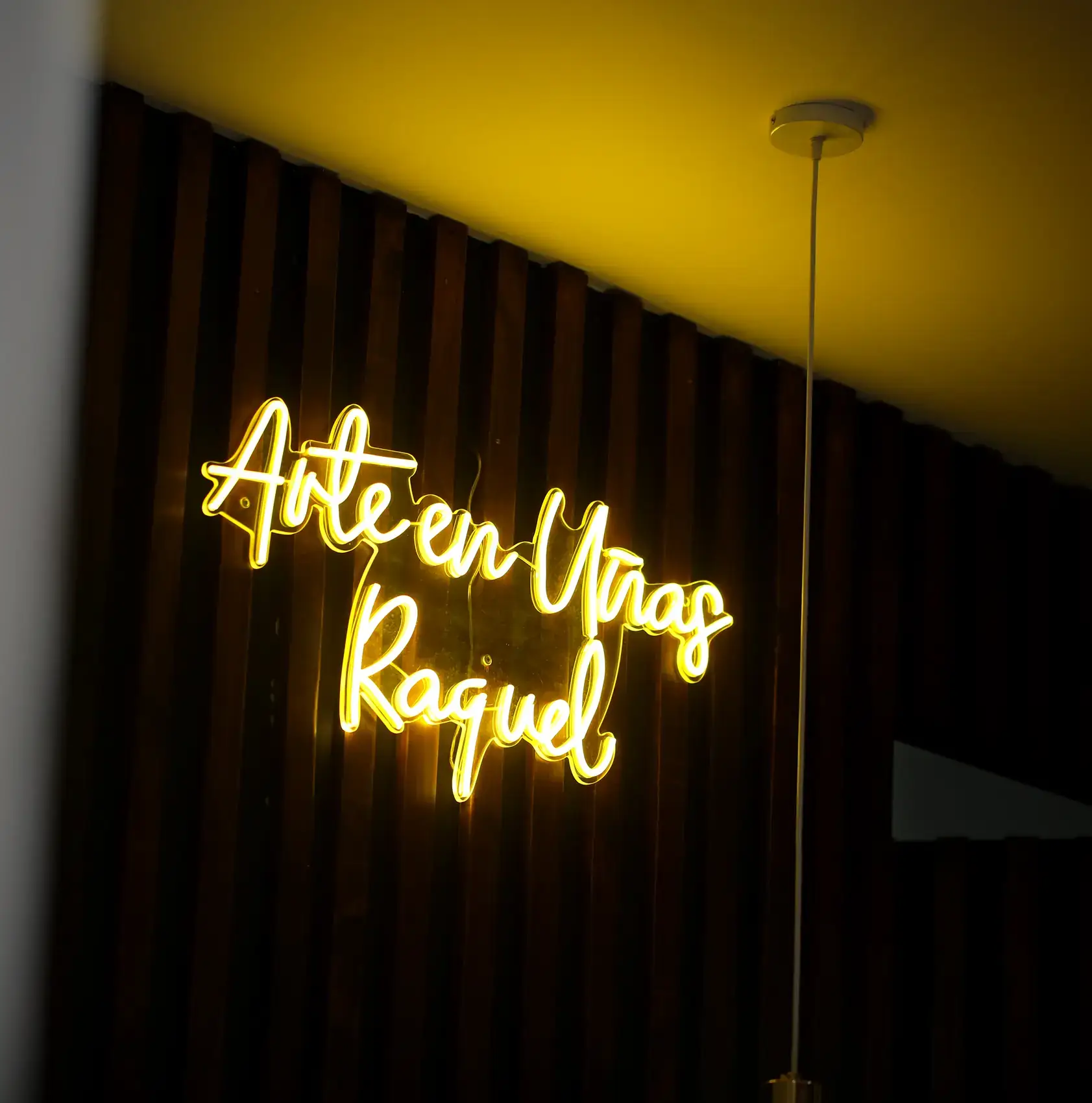 Letrero de neón «Arte en Uñas Raquel» en la pared de madera del salón
